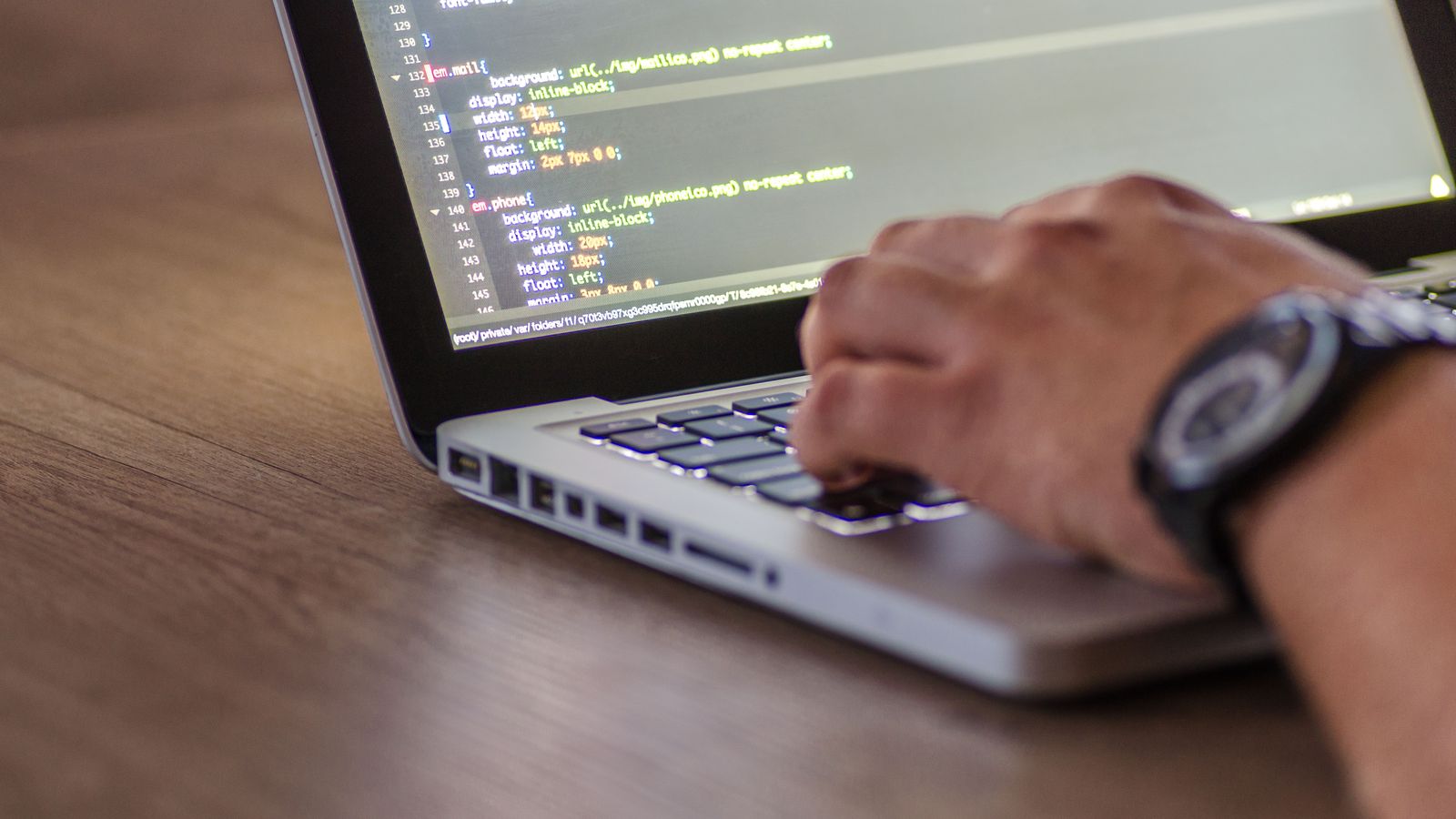 Hands typing code on a laptop showing CSS on the screen.